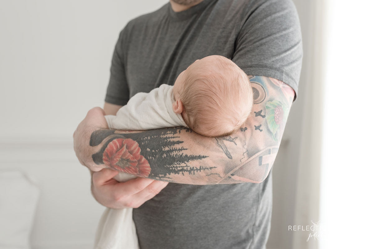 colour photo of dad holding newborn with tattoos