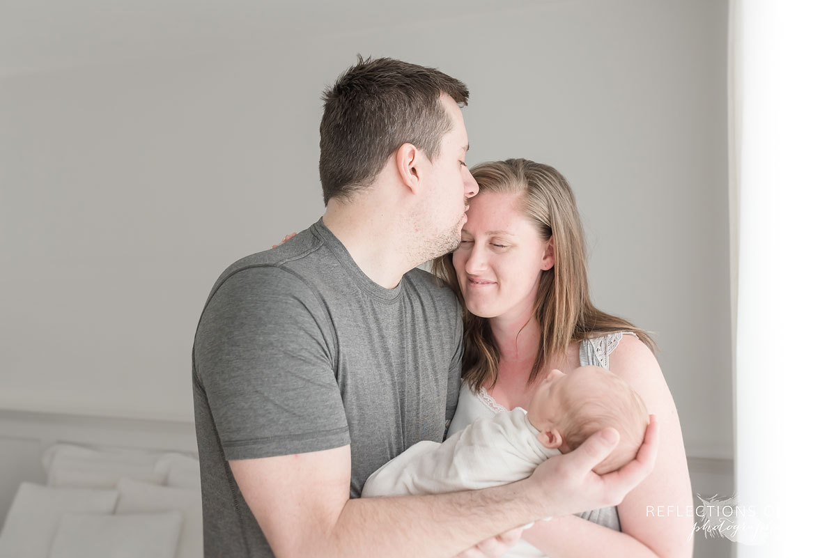 dad kissing mom on the forehead while holding newborn baby