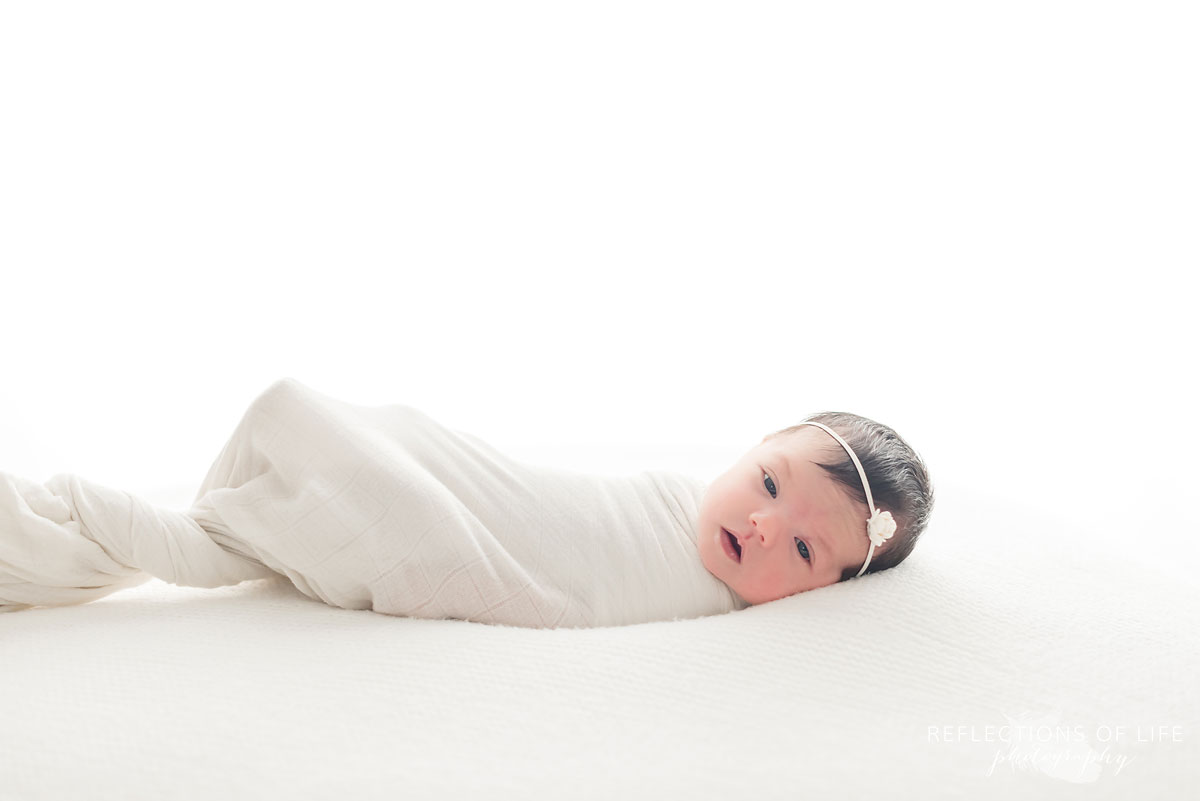 Newborn baby swaddled in white in white studio