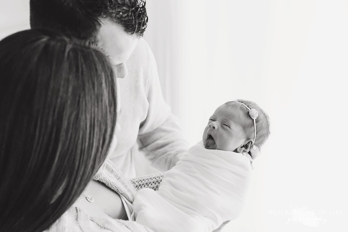 baby girl yawns in parents arms candid photography