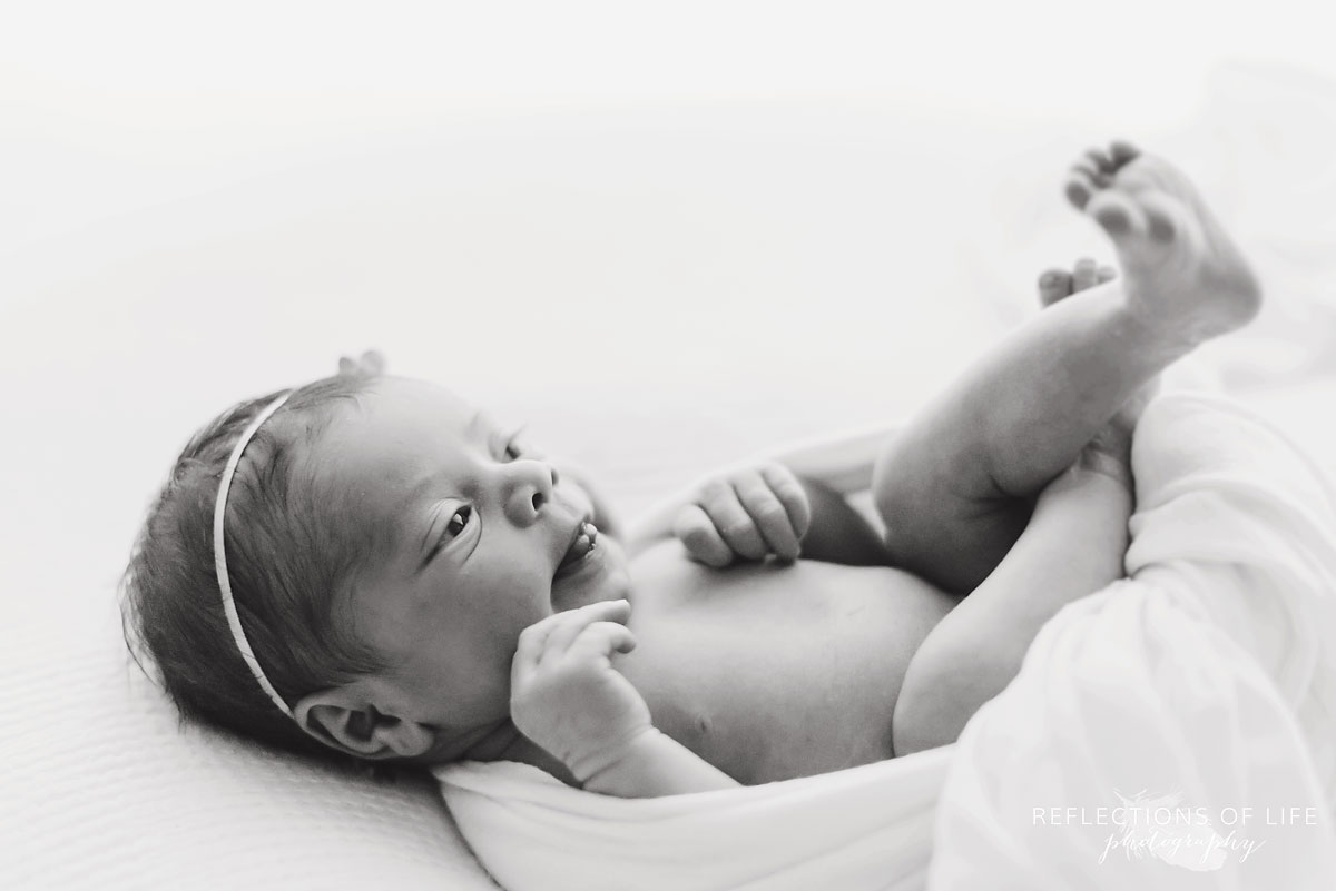 Newborn baby girl stretching with her tongue out in black and white