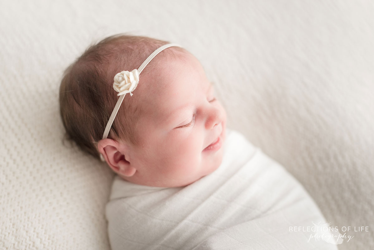 Newborn baby girl with simple white rose headband on beanbag