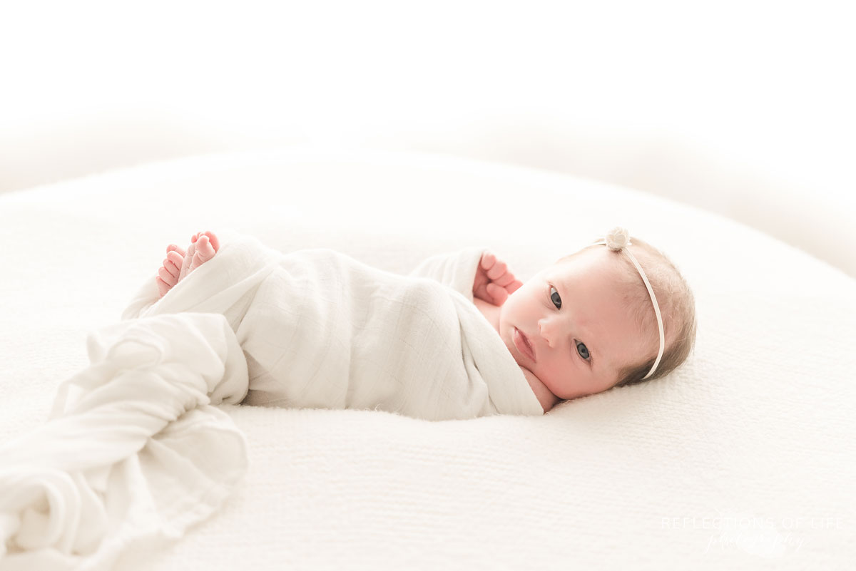 little newborn baby girl wrapped in white on white beanbag