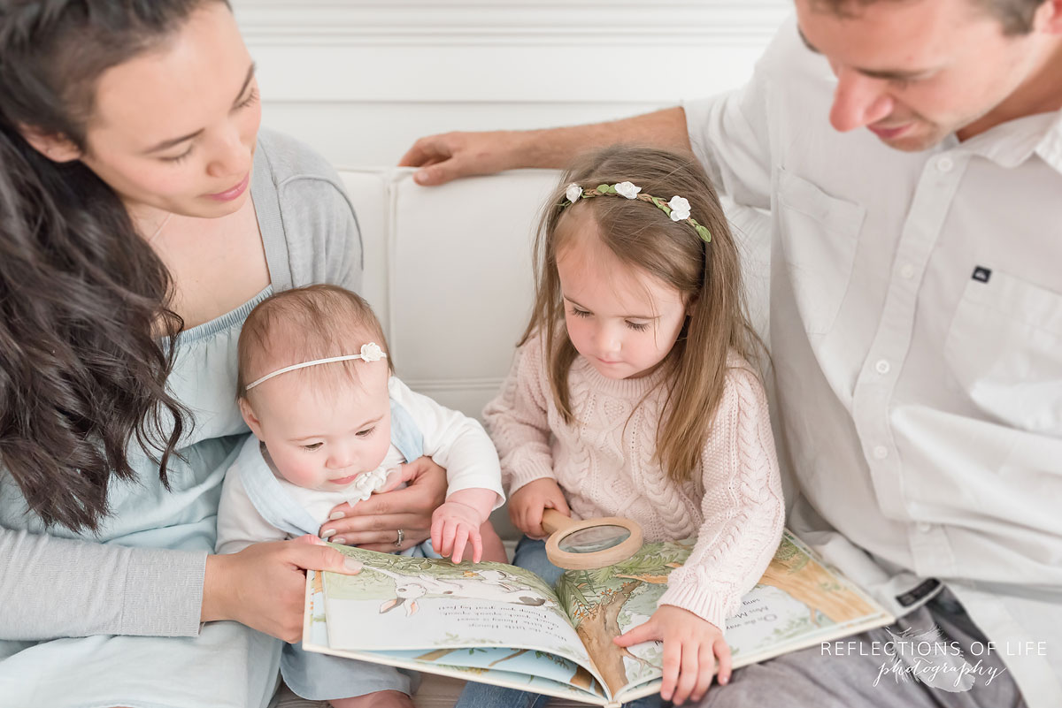 Family of four reading a book on a white couch