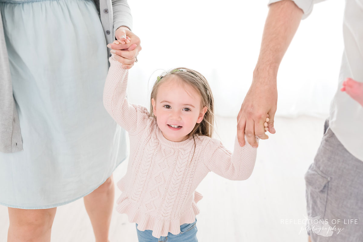Daughter holding mom and dad's hand in white studio