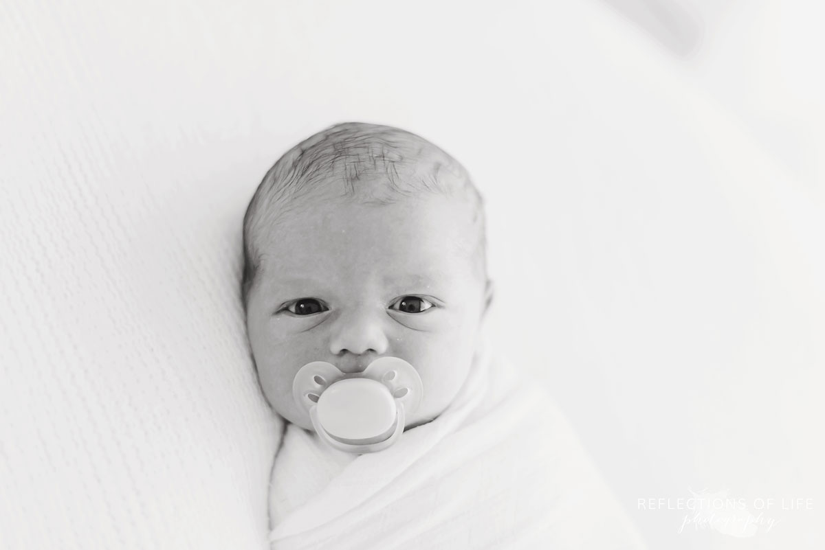 Baby boy with soother in his mouth looking at the camera