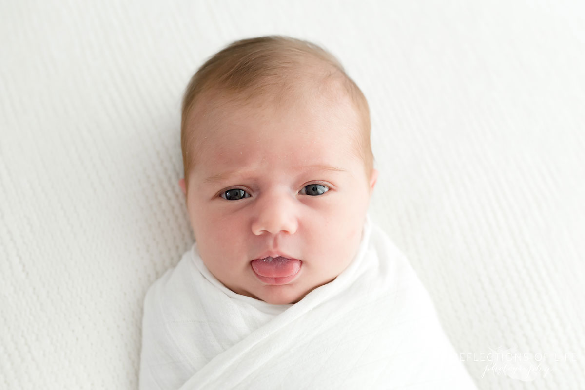 Baby sticking her tongue out on white blanket