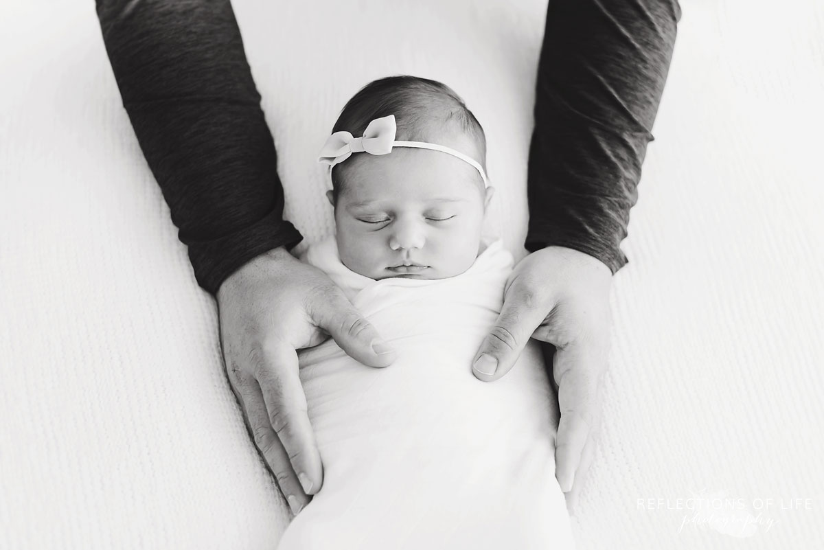 Father putting his hands on baby girl with bow black and white