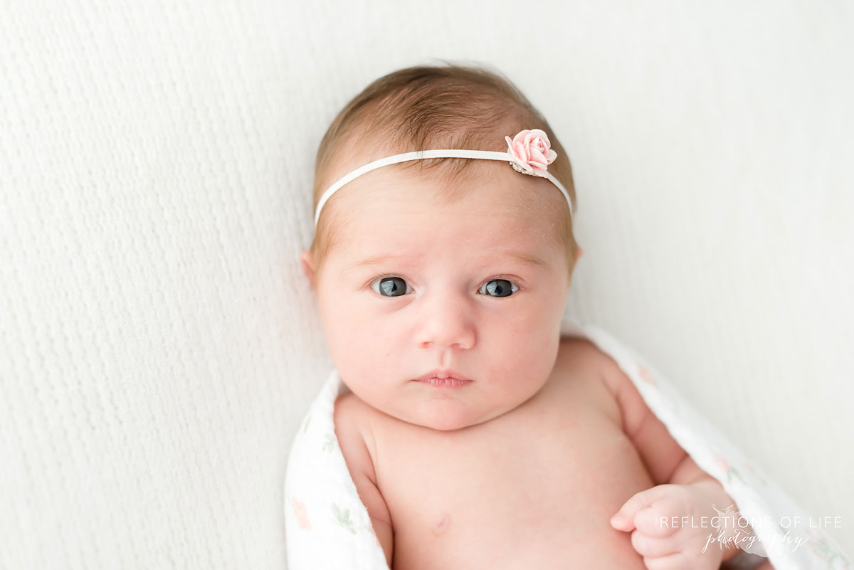 Baby girl with flower headband looking at camera in white studio