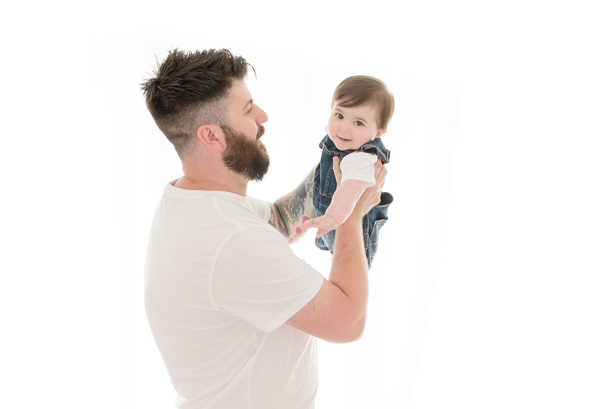 Dad holding up his baby in white studio