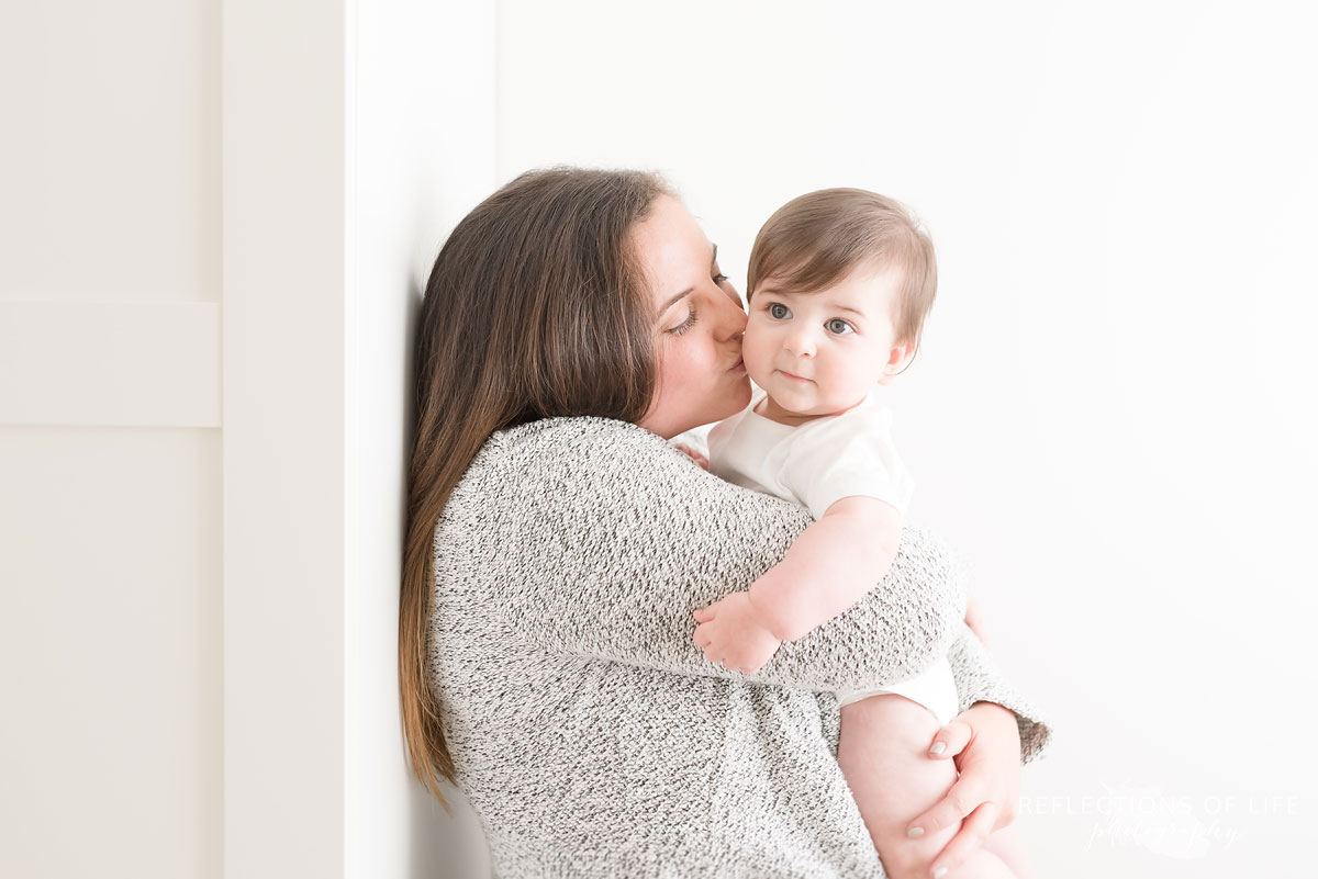Mother kissing baby on cheek white holding baby up