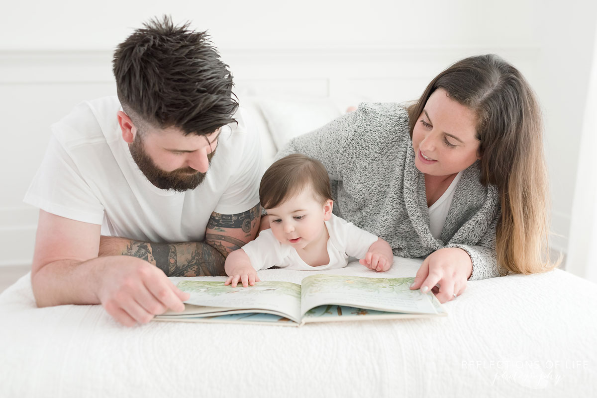 Mom and dad reading a book to baby on white couch