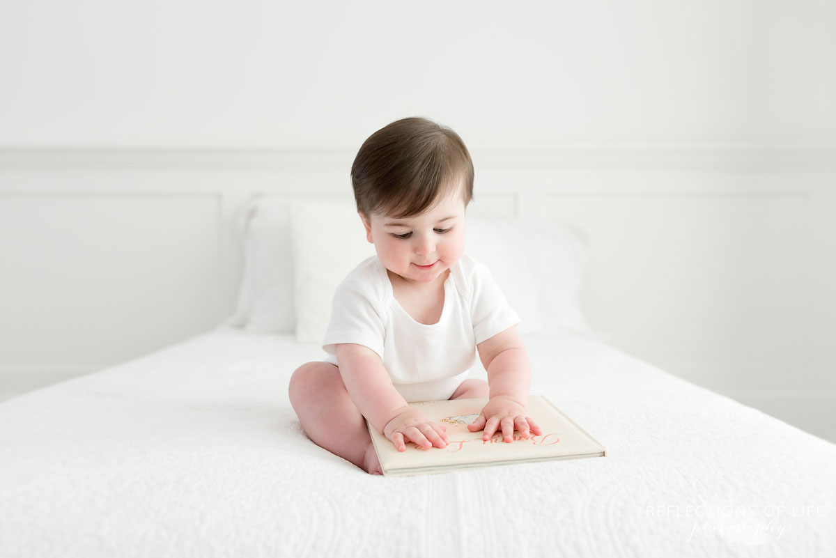 Baby looking at cover of book on white couch Grimsby Ontario