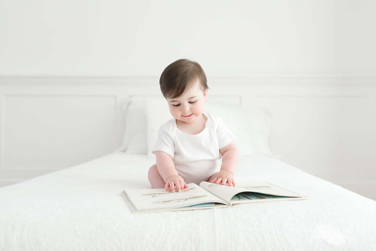 Baby looking at book pages on white couch Niagara Photography