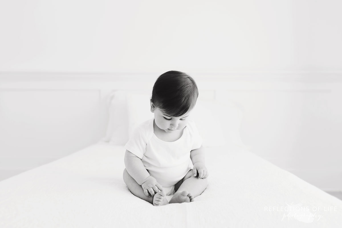 Baby looking at toes on white couch black and white