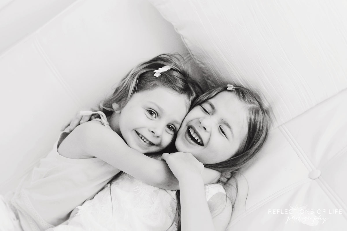 two sisters hugging each other while laying on couch