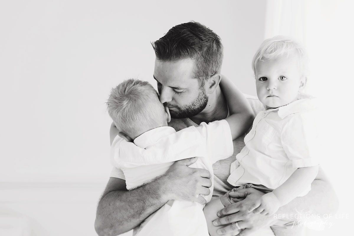 father hugging two sons in studio black and white