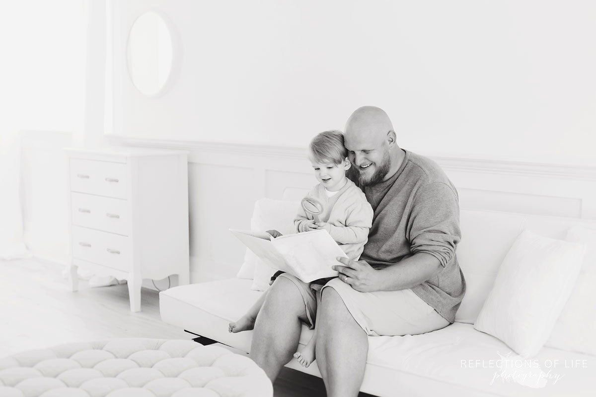 father reading to son on white couch in studio black and white