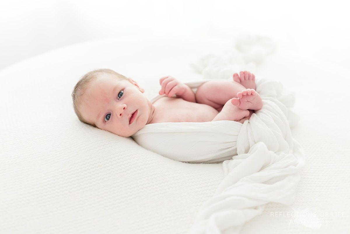 portrait of newborn baby boy sitting on pillow wrapped in a blanket