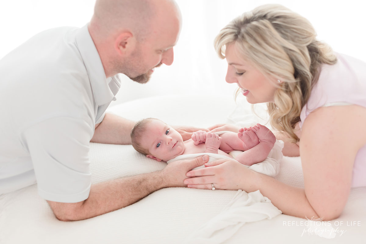mom and dad holding baby on pillow in studio