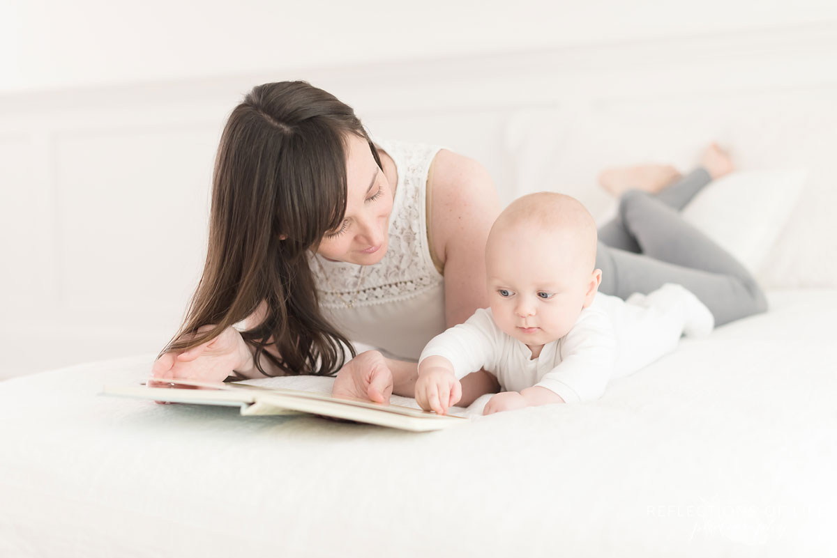 baby and mother laying on bed in studio with book.jpg
