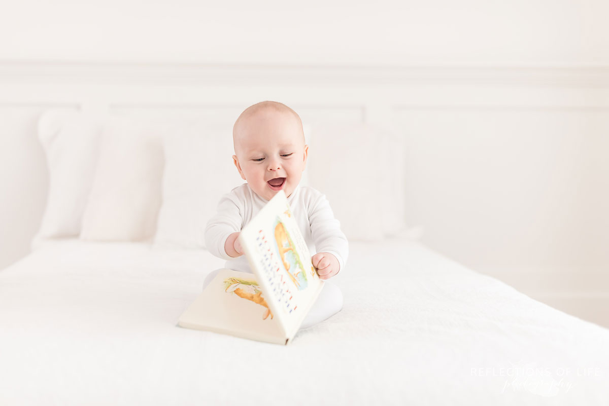 baby boy laying on white bed with book.jpg