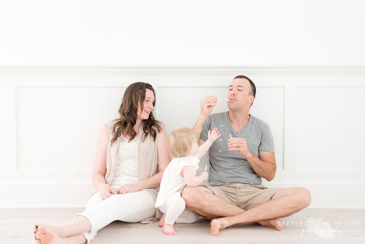 dad blows bubbles for his little girl in neutral light studio