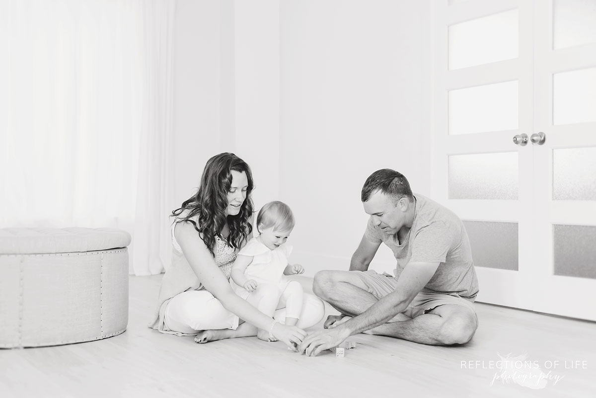 Beautiful family sitting on the studio floor playing with blocks in black and white