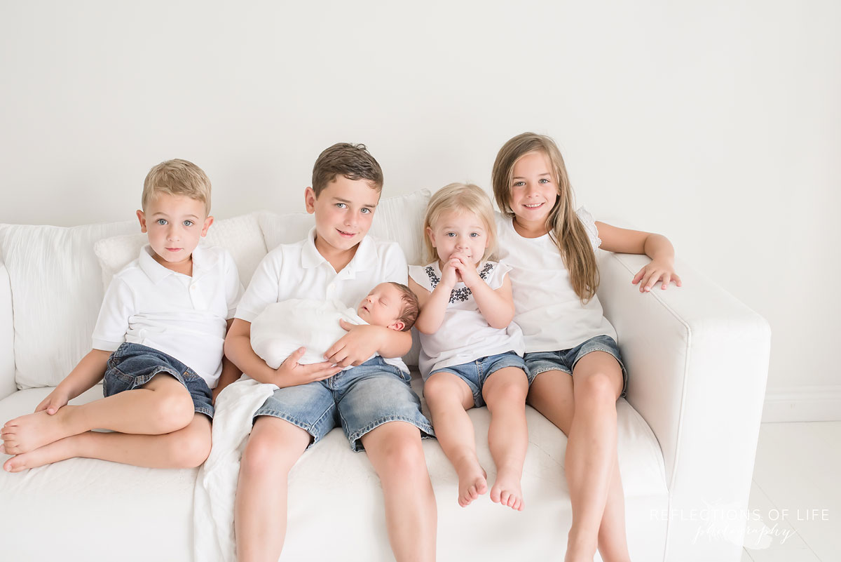 Family of 5 siblings hold their new baby brother on the couch