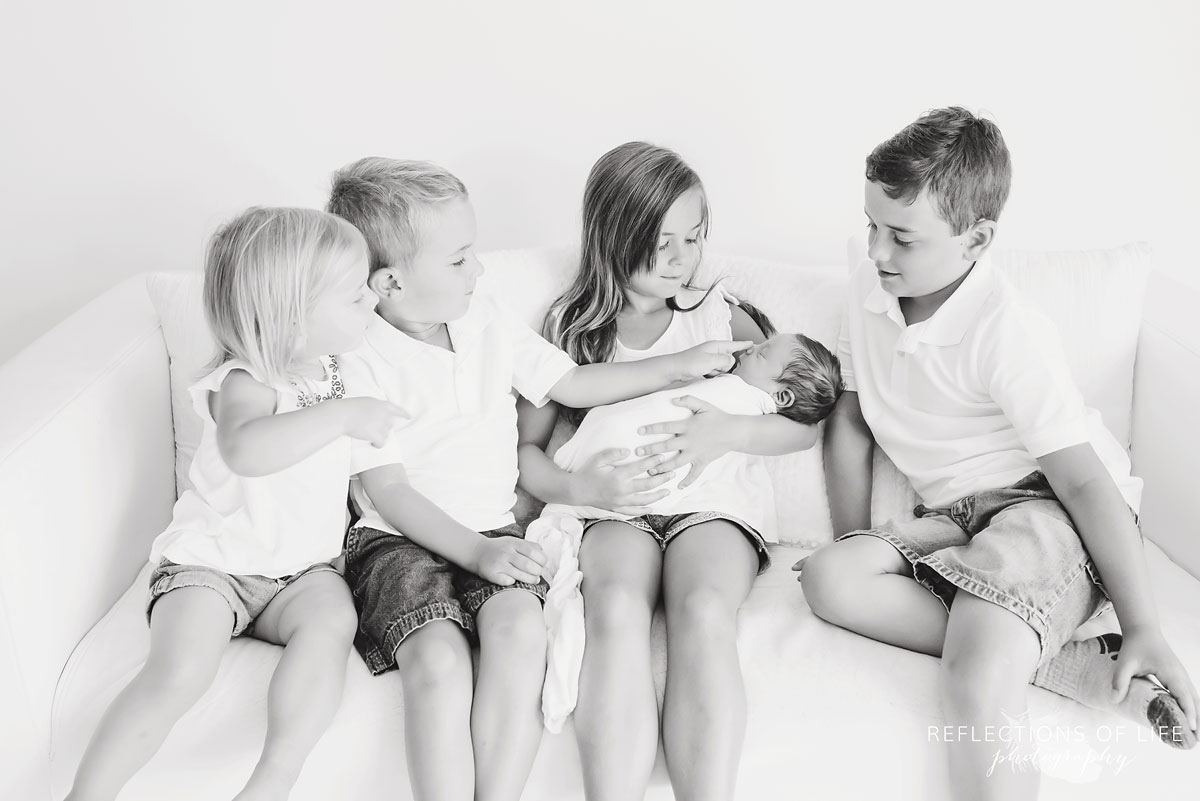4 siblings hold new baby brother on sofa