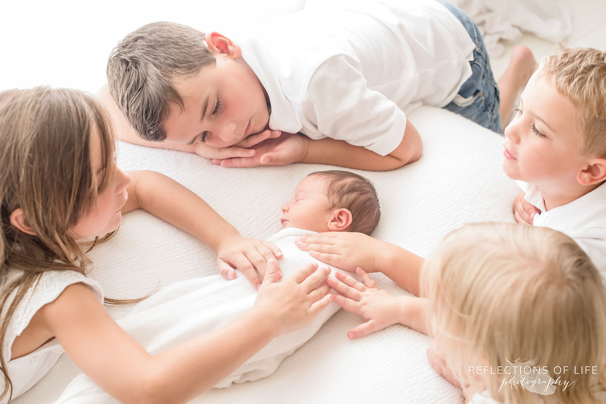 siblings laying hands on their newborn baby brother