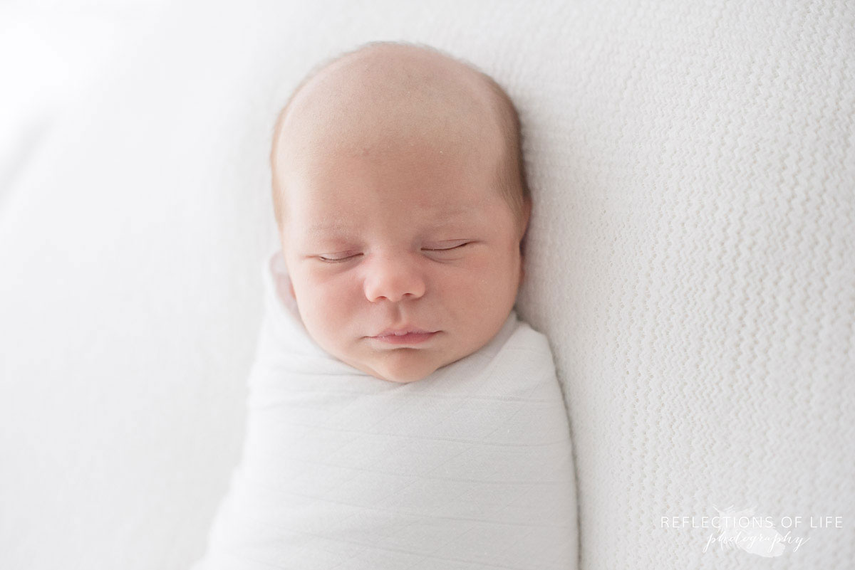 Adorable newborn baby boy wrapped in Little Unicorn swaddle blanket