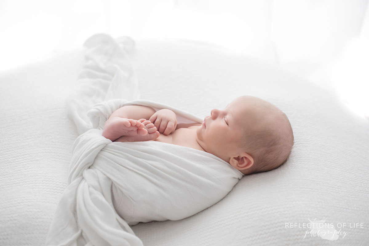Newborn baby boy swaddled in white Little Unicorn muslin blanket