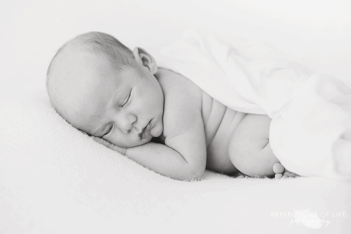 Black and white image of newborn baby with white muslin blanket