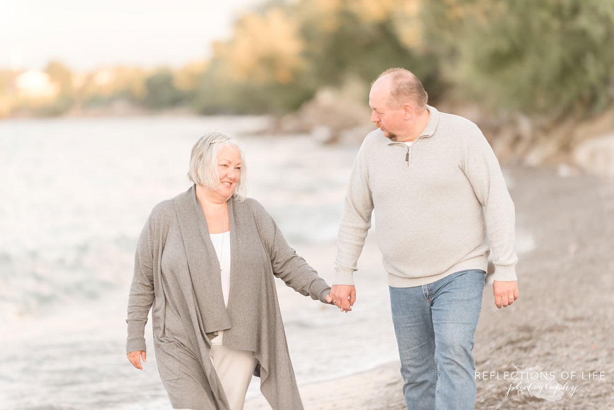 Husband and wife holding hands and walking along the beach in Niagara Region