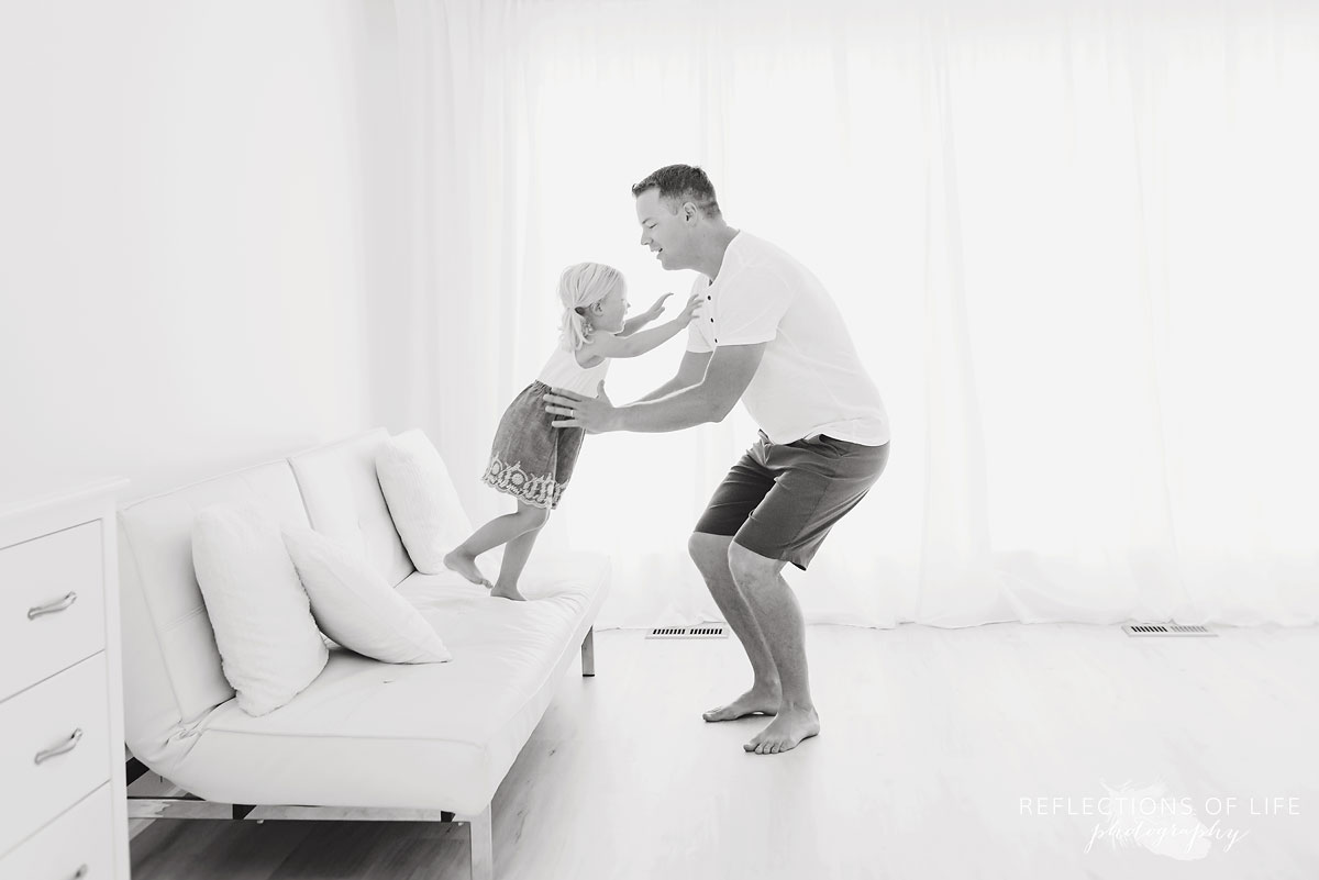 Girl jumping into daddys arms off white couch