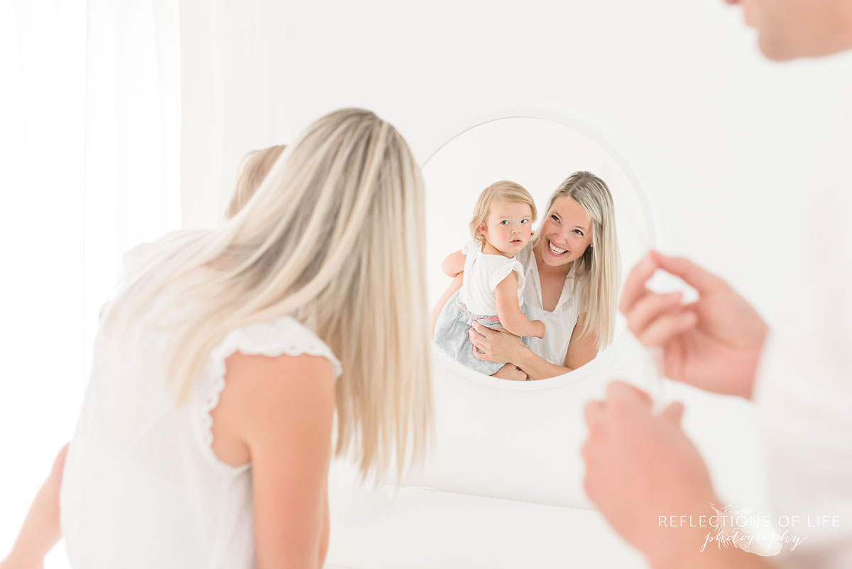 mother and daughter looking into mirror in white studio