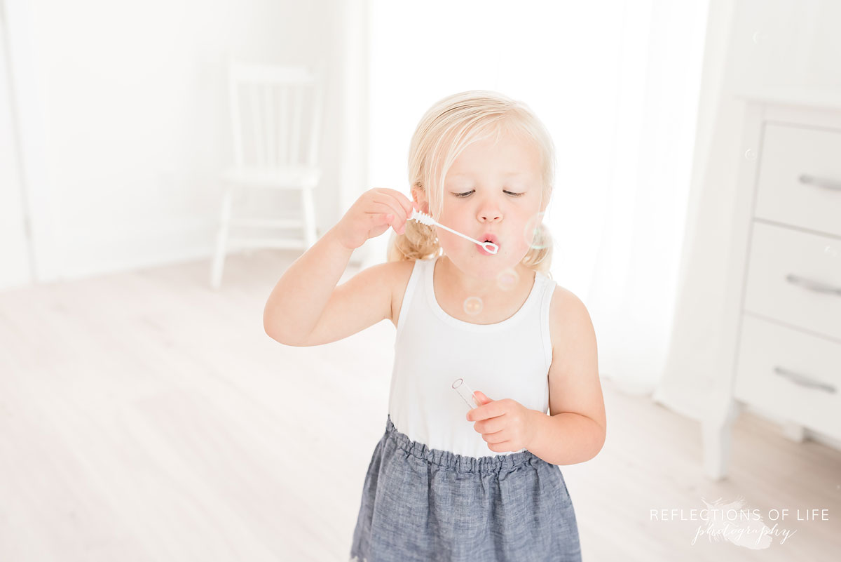 little girl blowing bubbles in white studio