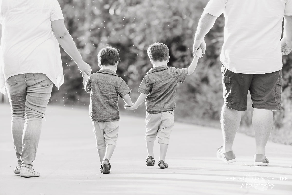 Family of four holding hands and walking down a path black and white