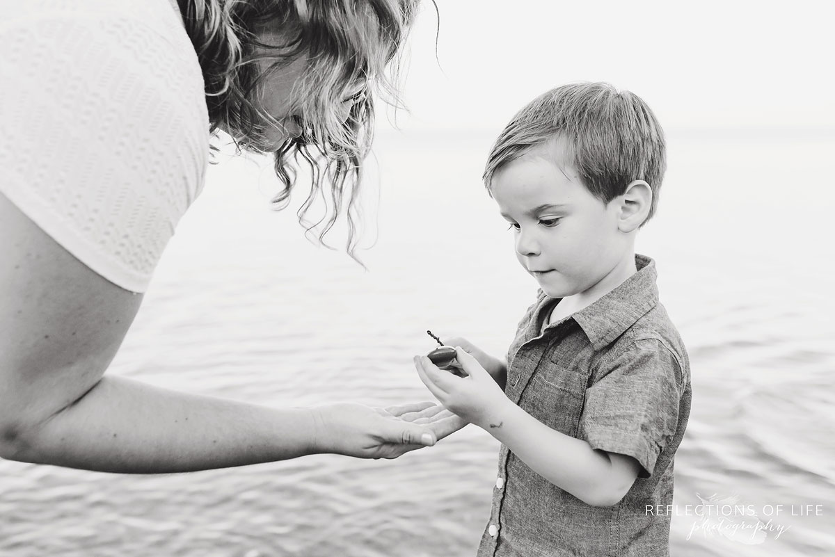 Mother holding her hand out looking at son who is holding a rock black and white