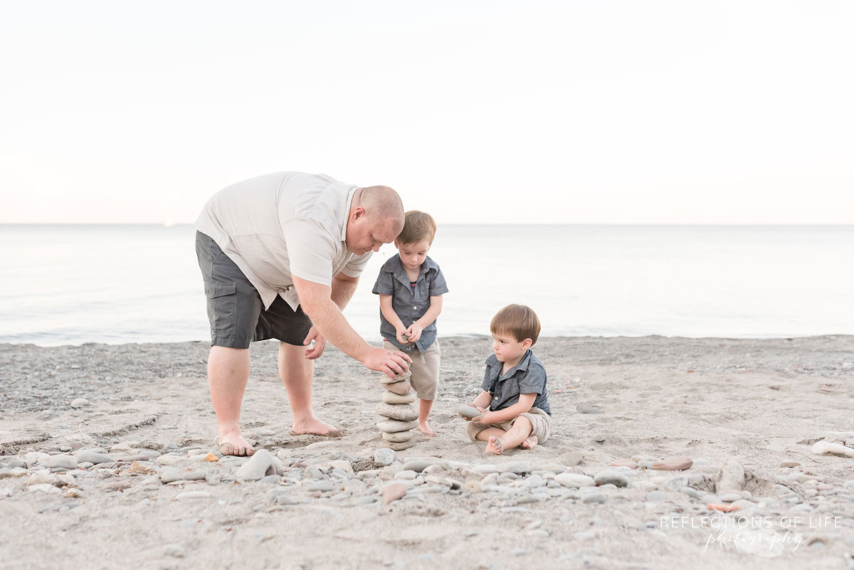 Father and two sons building a rock tower on Grimsby Beach