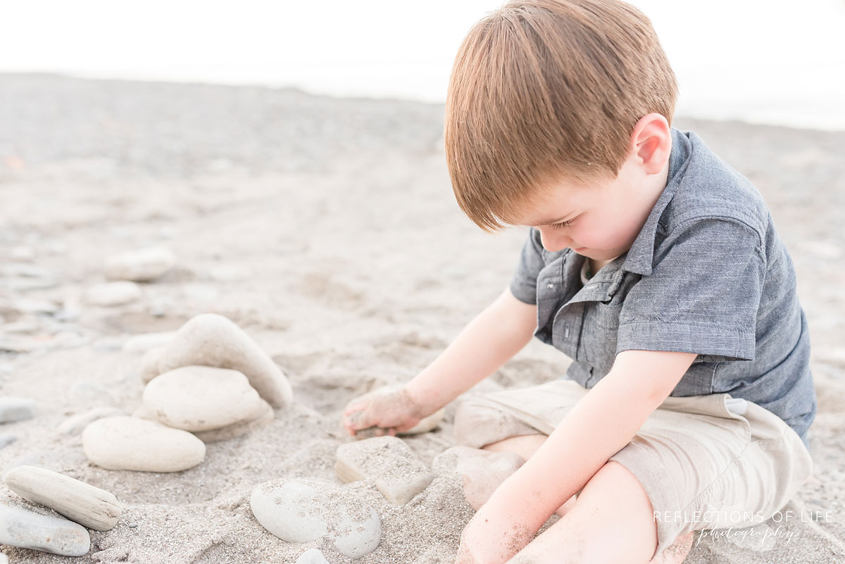 boy sitting on the sand playing with rocks