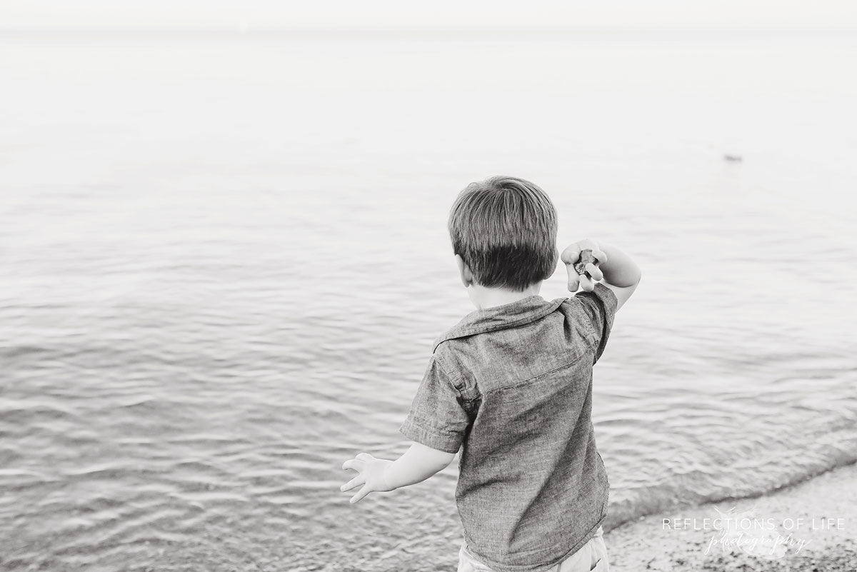 boy throwing a rock into the water black and white