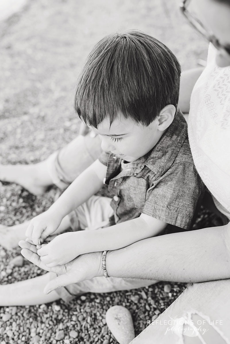 mom and son sitting together on the beach playing with stones black and white