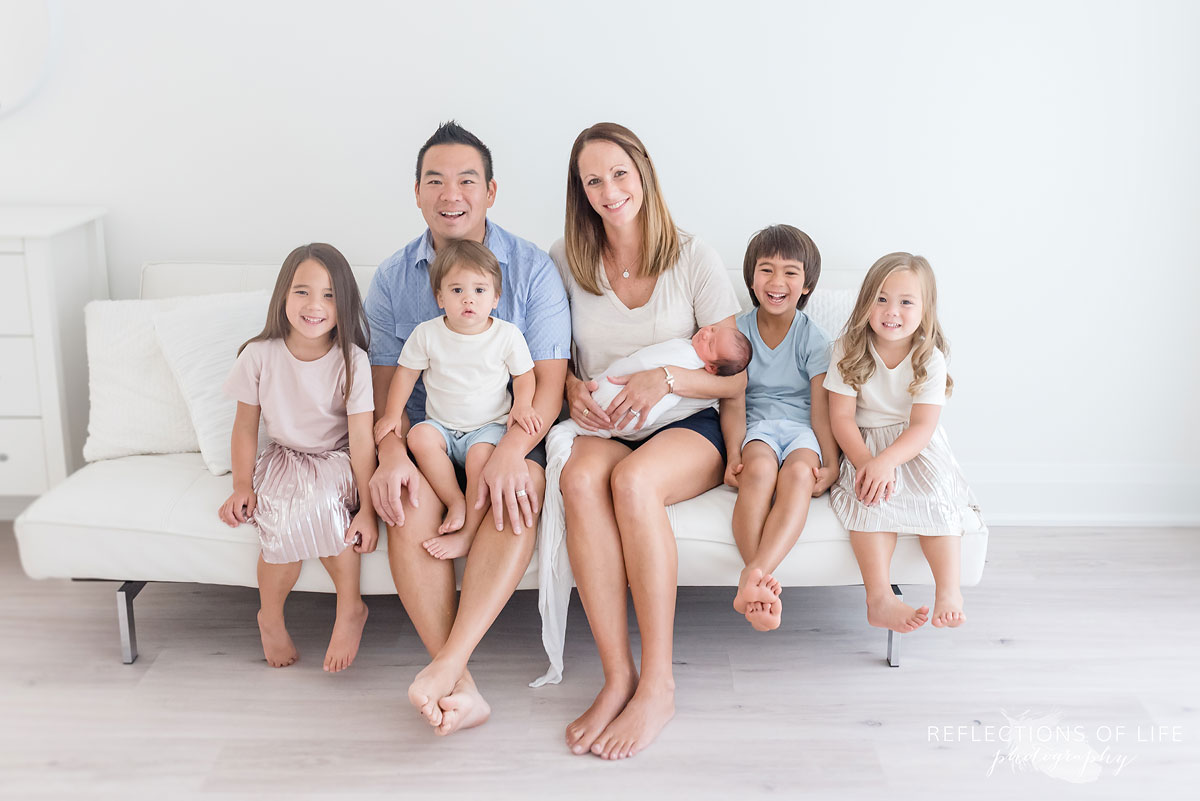family of seven sitting on a couch in a studio smiling