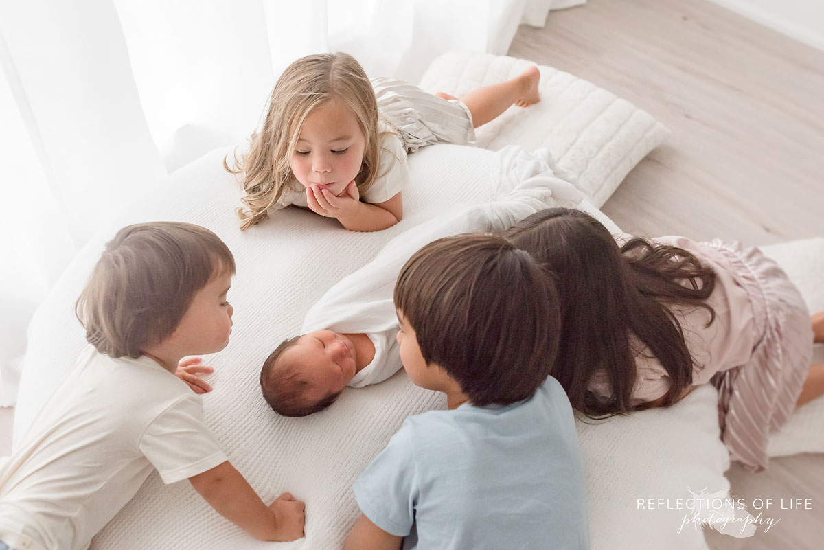 four children look at their baby sibling sleeping
