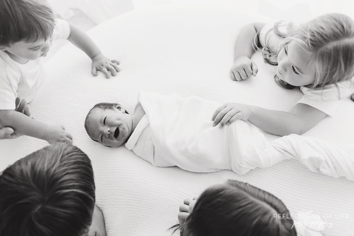 four children looking down at their newborn sibling laughing black and white