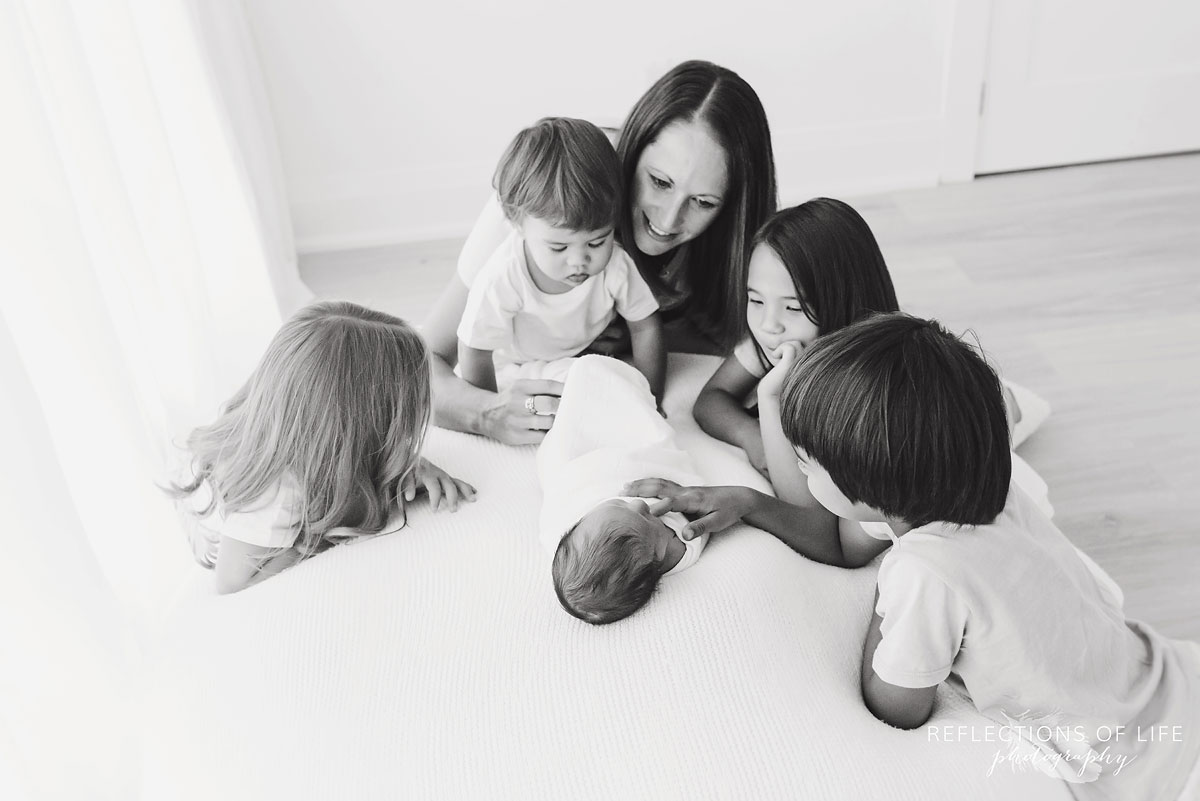 four children and mom look at their baby sibling at Reflections of Life Photography studio black and white