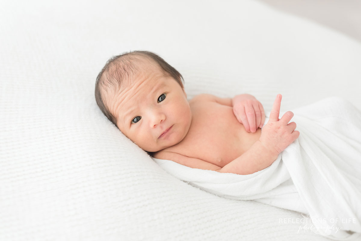 newborn boy looking to the side pointing upwards while laying down