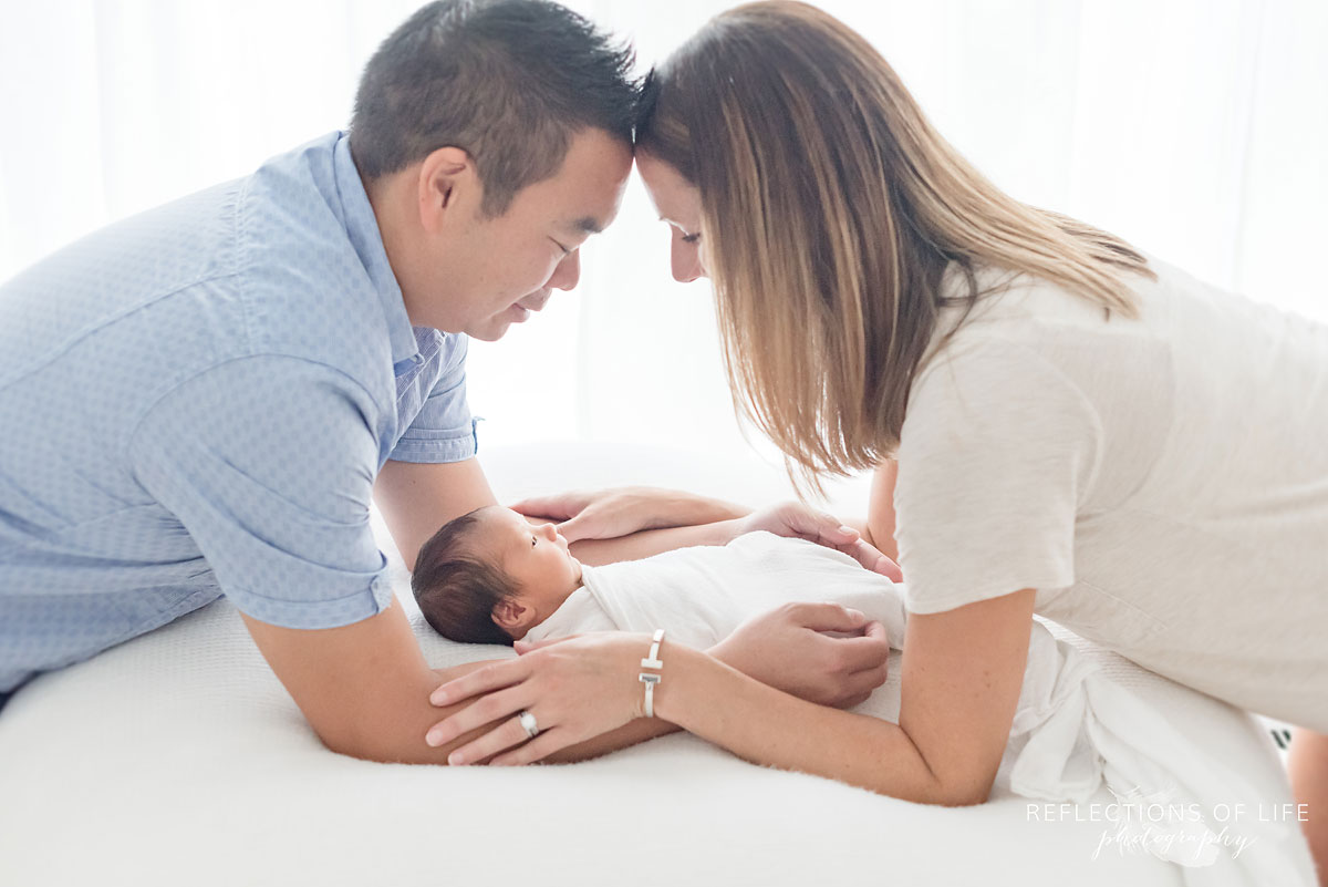 loving couple holding each other touching heads with newborn baby son between them